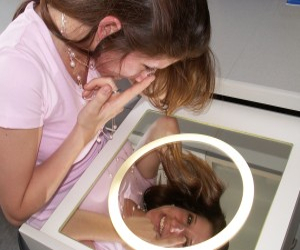 junge Frau setzt Kontaktlinsen vor waagerechtem Spiegel ein