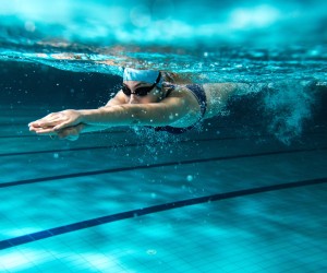 junge Frau schwimmt in einem Schwimmbad nach links aus dem Bild, Unterwasserphoto